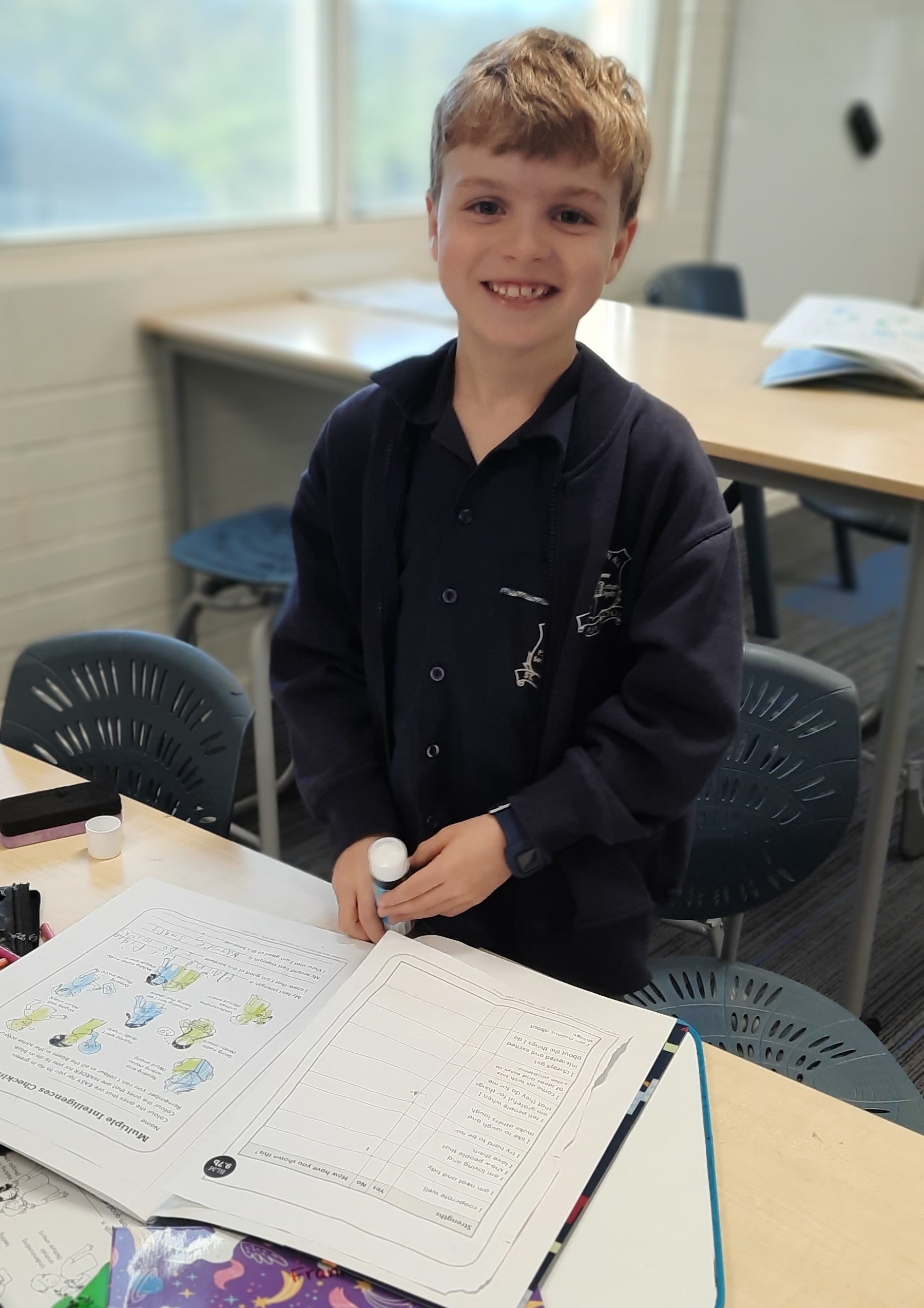 Student smiling while completing classroom learning tasks, highlighting confidence engagement and a positive learning experience at St Pius X Primary School