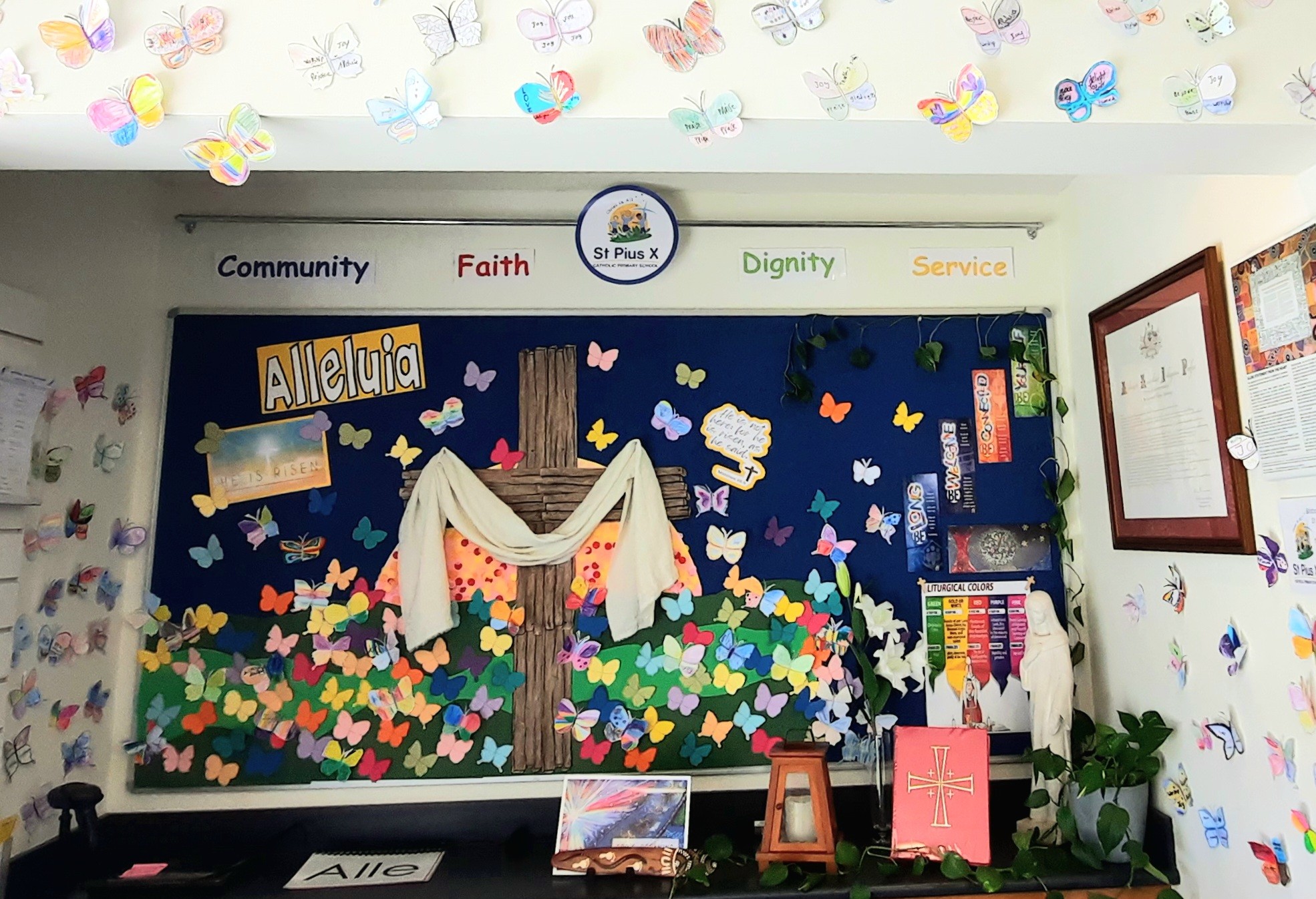 Prayer and reflection display at St Pius X Primary School featuring a cross with Alleluia message and student created butterflies, highlighting Catholic faith, celebration and student participation in shared spiritual life