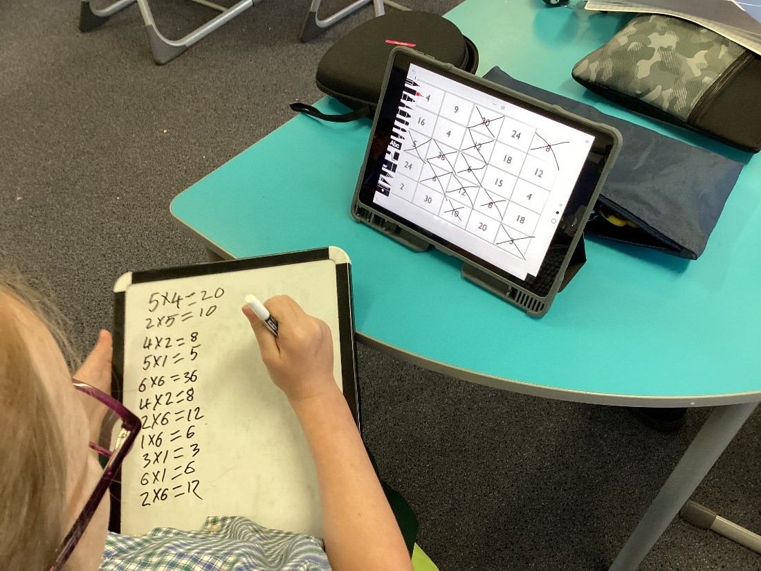 Student solving maths problems using a whiteboard alongside a tablet, highlighting problem solving, independent learning and digital integration at St Pius X Primary School